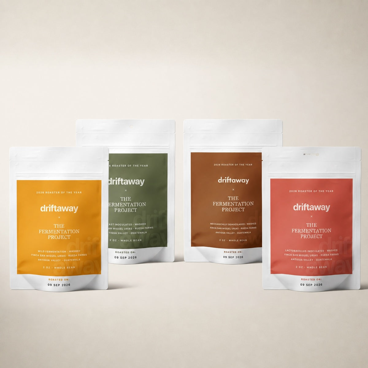 Four stand-up pouches of Driftaway fermentation products arranged in a row against a warm beige background. The pouches are white with large color blocks in mustard yellow, olive green, terracotta brown, and coral red, with white text.
